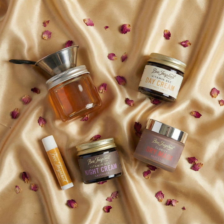 Skincare products including jars and a lip balm on a beige fabric background with dried flowers