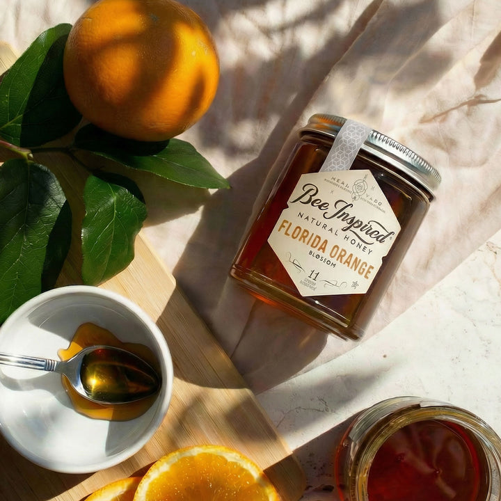 Jar of 'Bee Inspired' Florida Orange honey with oranges and a spoon on a light surface