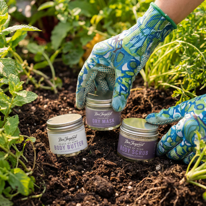 Person wearing gardening gloves with skincare products in a garden setting