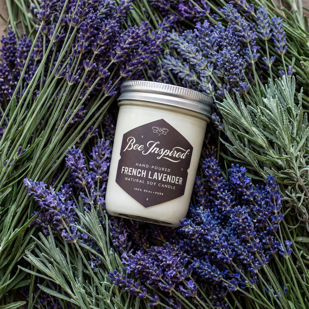 Candle jar labeled 'Bee Inspired' surrounded by lavender flowers