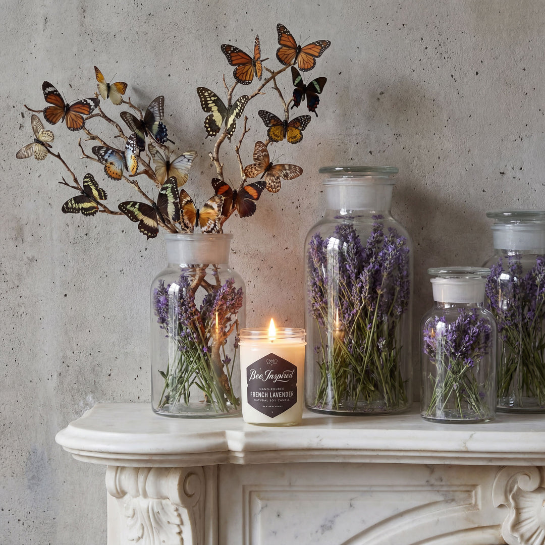 Decorative setup with glass jars containing lavender, a lit candle, and a metal butterfly branch on a marble surface.