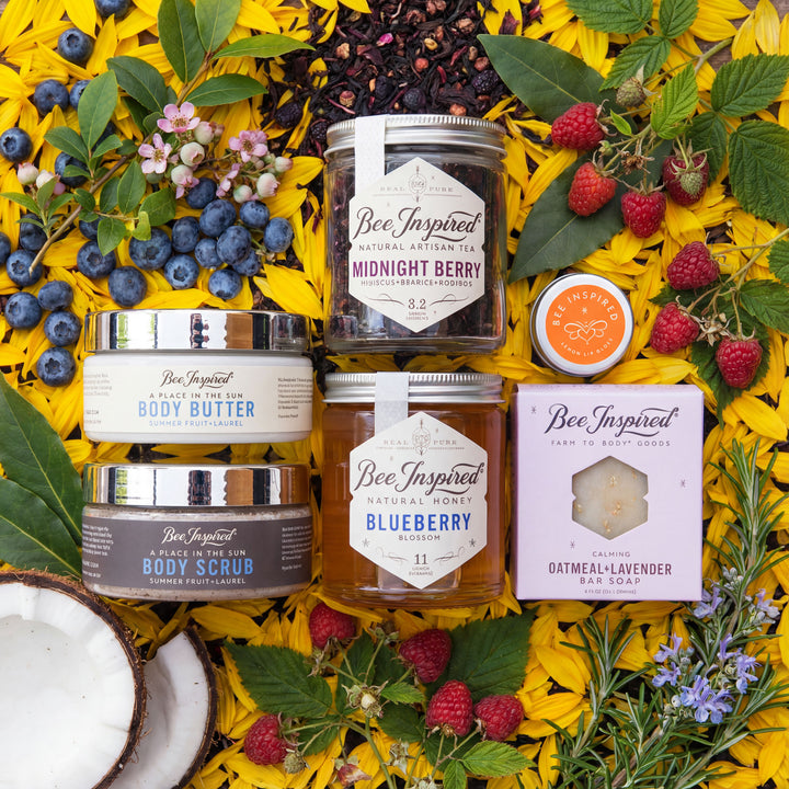 Collection of 'Bee Inspired' natural products including tea, body butter, scrub, honey, and soap on a floral background.
