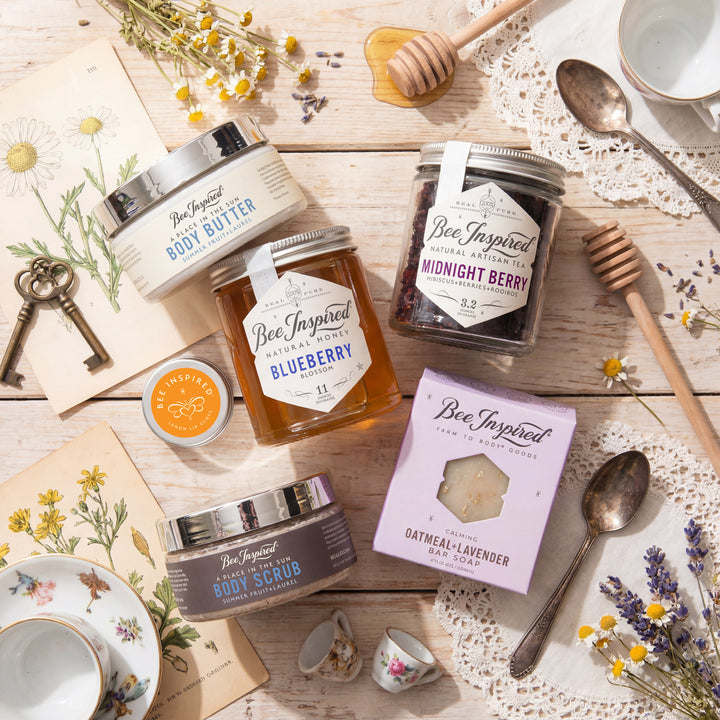 Bee-Inspired products including body butter, honey, and scrub on a wooden surface with flowers and spoons.
