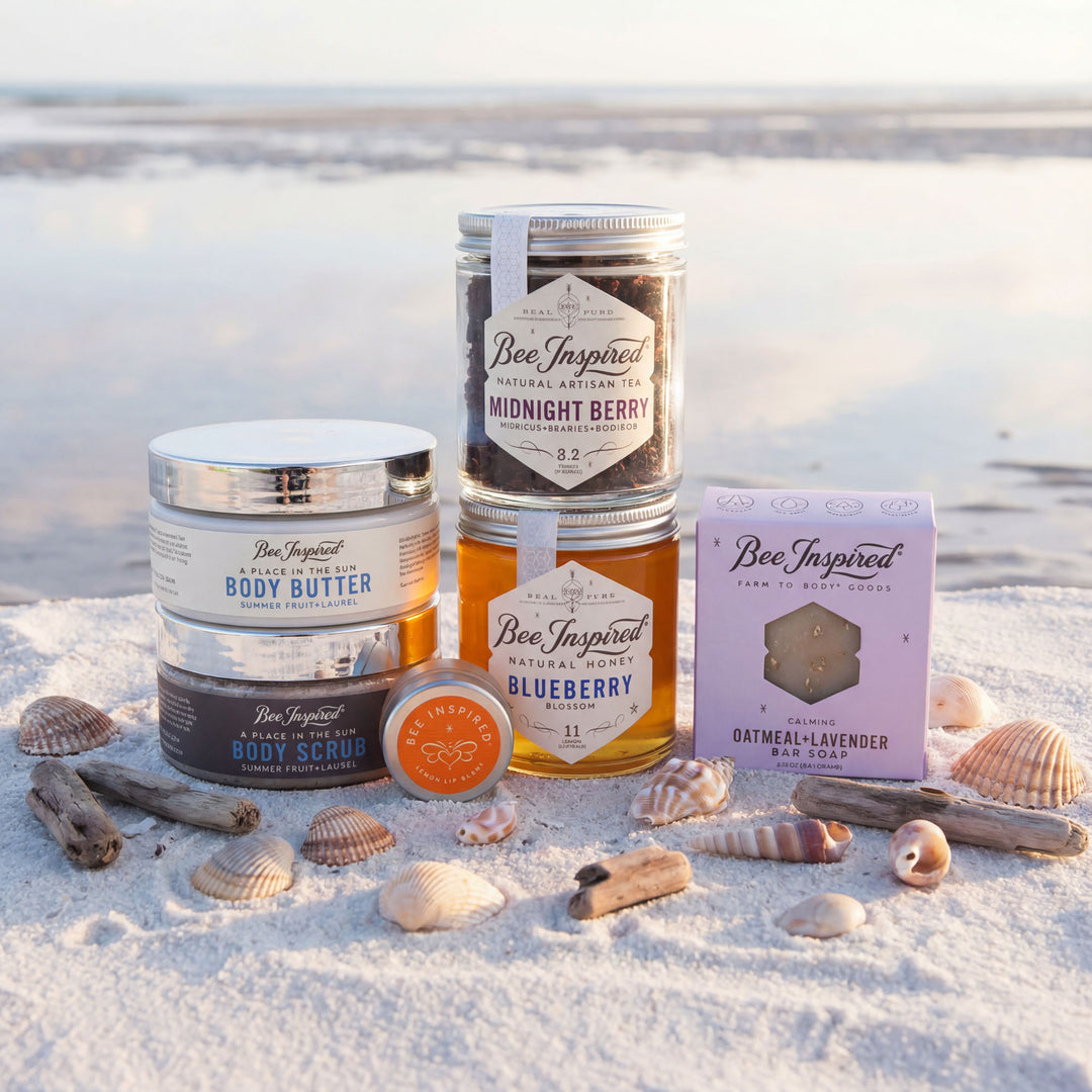 Bee Inspired product lineup including jars, a box, and a bar on a sandy beach with seashells.