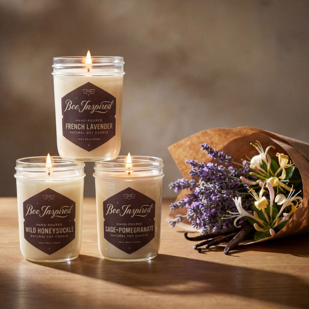 Three 'Bee Inspired' candles on a wooden surface with a bouquet of lavender and vanilla beans.
