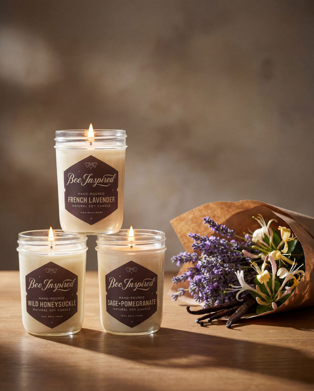 Three candles with labels and a bouquet of lavender on a wooden surface.