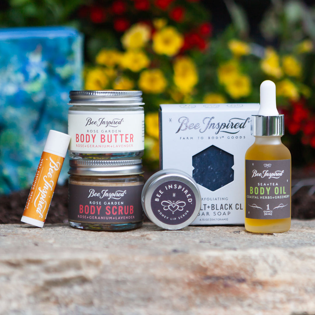 Collection of Bee Inspired skincare products on a stone surface with a blurred floral background