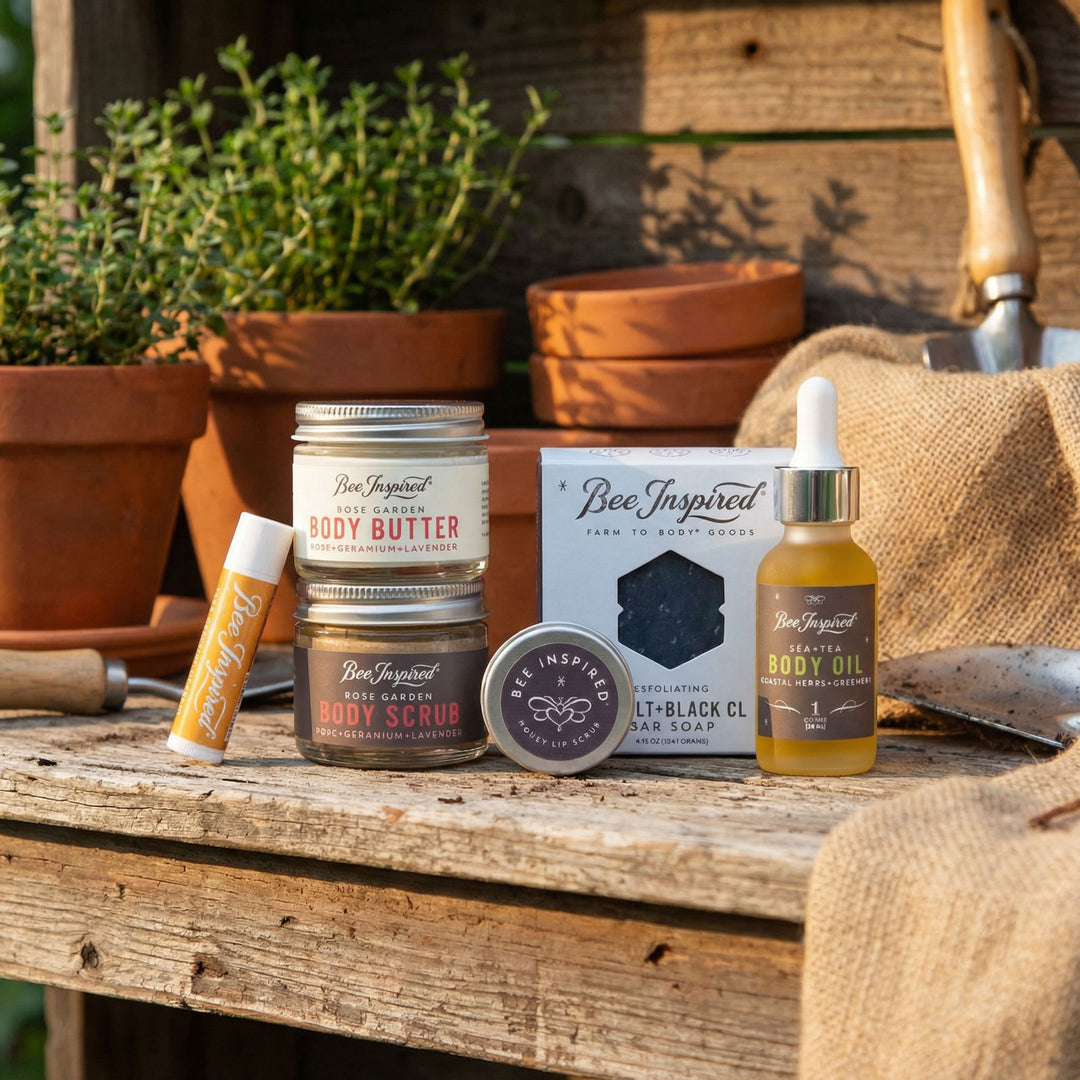 Collection of Bee Inspired products including body butter, oil, and soap on a wooden surface with plants in the background.