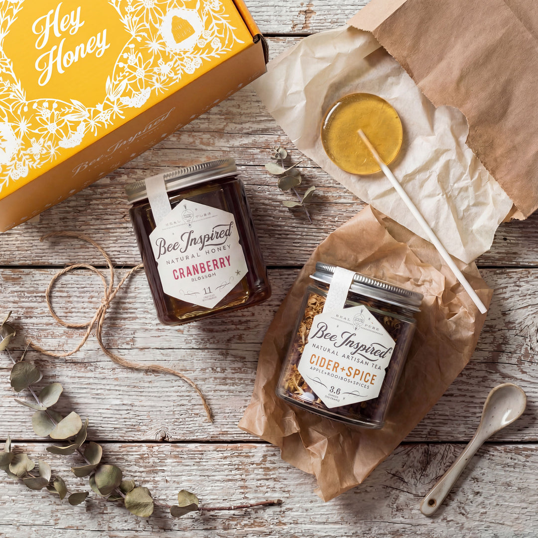 Two jars of 'Bee Inspired' honey on a wooden surface with a decorative box and lemon.