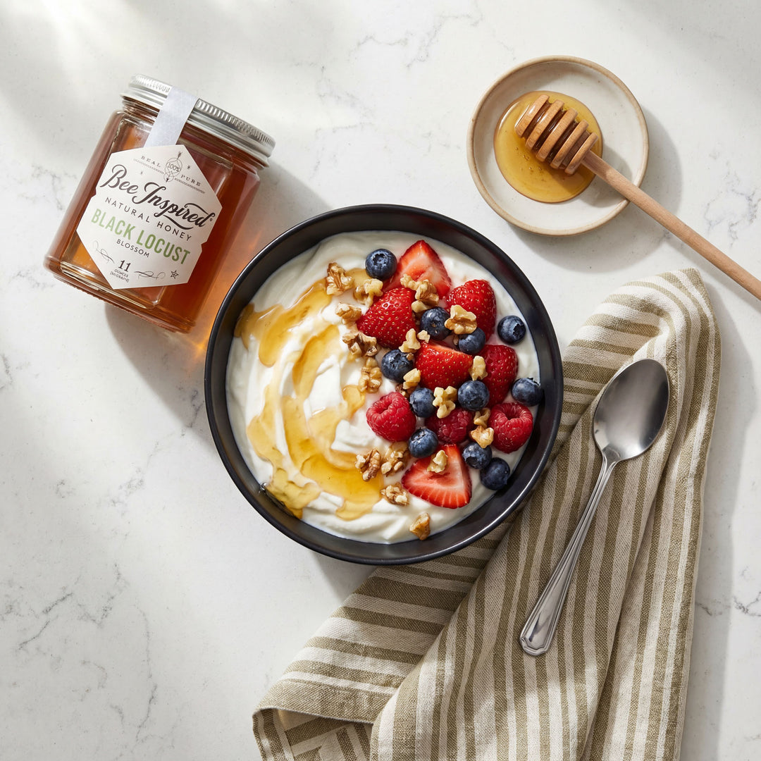 Yogurt bowl with berries, nuts, and honey next to a jar of honey on a marble surface.