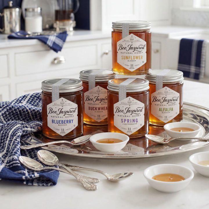 Jars of 'Bee Inspired' honey on a tray with spoons and small bowls in a kitchen setting.
