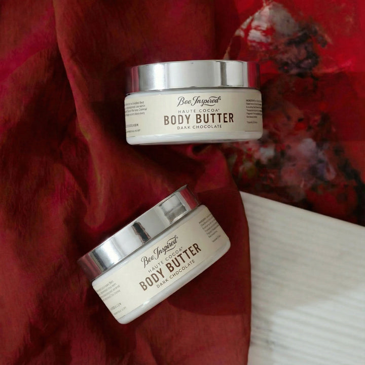 Two jars of Haute Cocoa Body Butter on a red fabric background