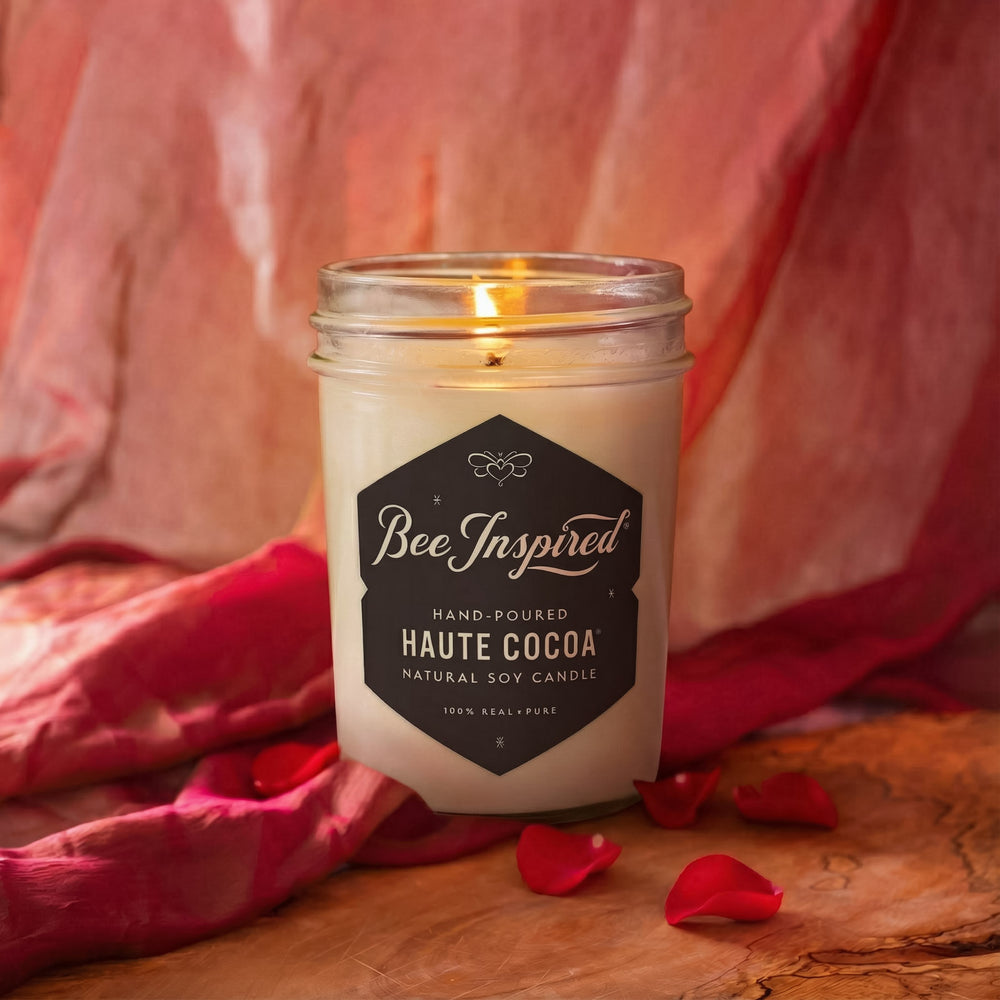 Candle in a mason jar with 'Bee Inspired' label on a wooden surface with pink fabric in the background