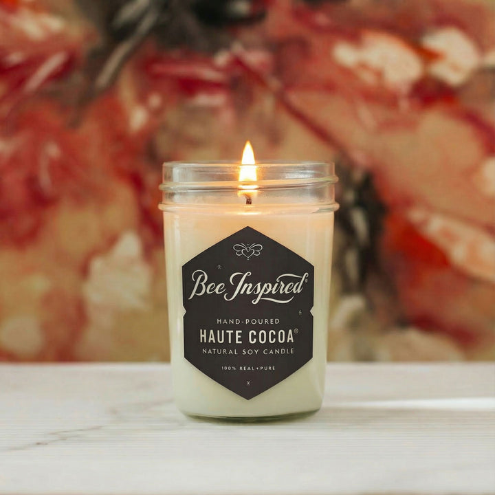 Bee Inspired jelly jar candle in Haute Cocoa scent on white table with blurred red background