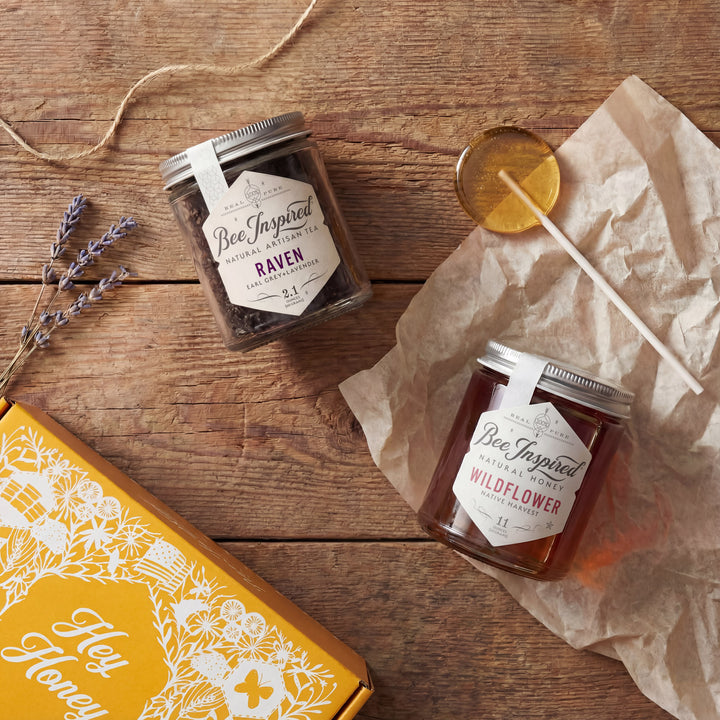 Two jars of honey with labels on a wooden surface, accompanied by lavender and a box.
