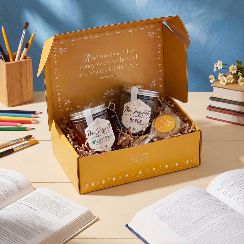 Gift box with honey jars and a cookie on a wooden table with books and stationery.