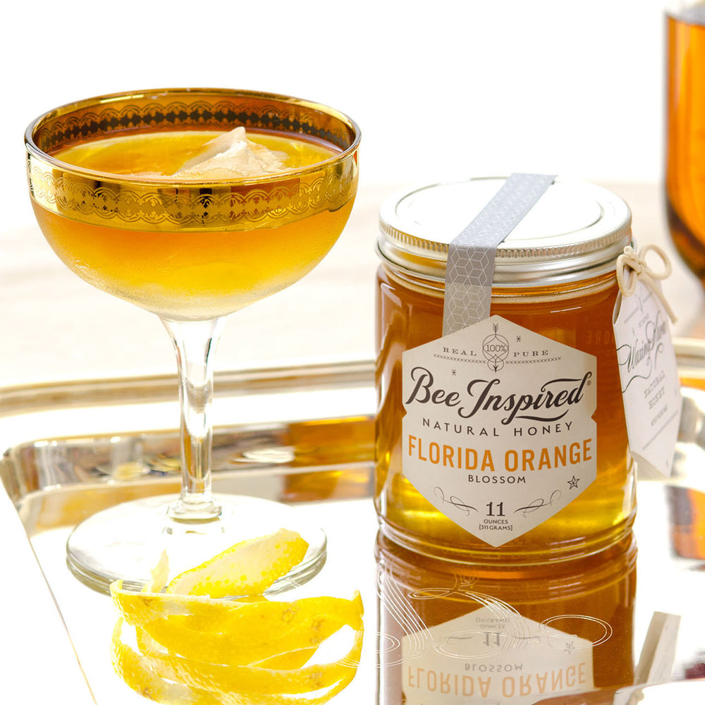 bee inspired florida orange blossom honey on a tray next to a cocktail made with it