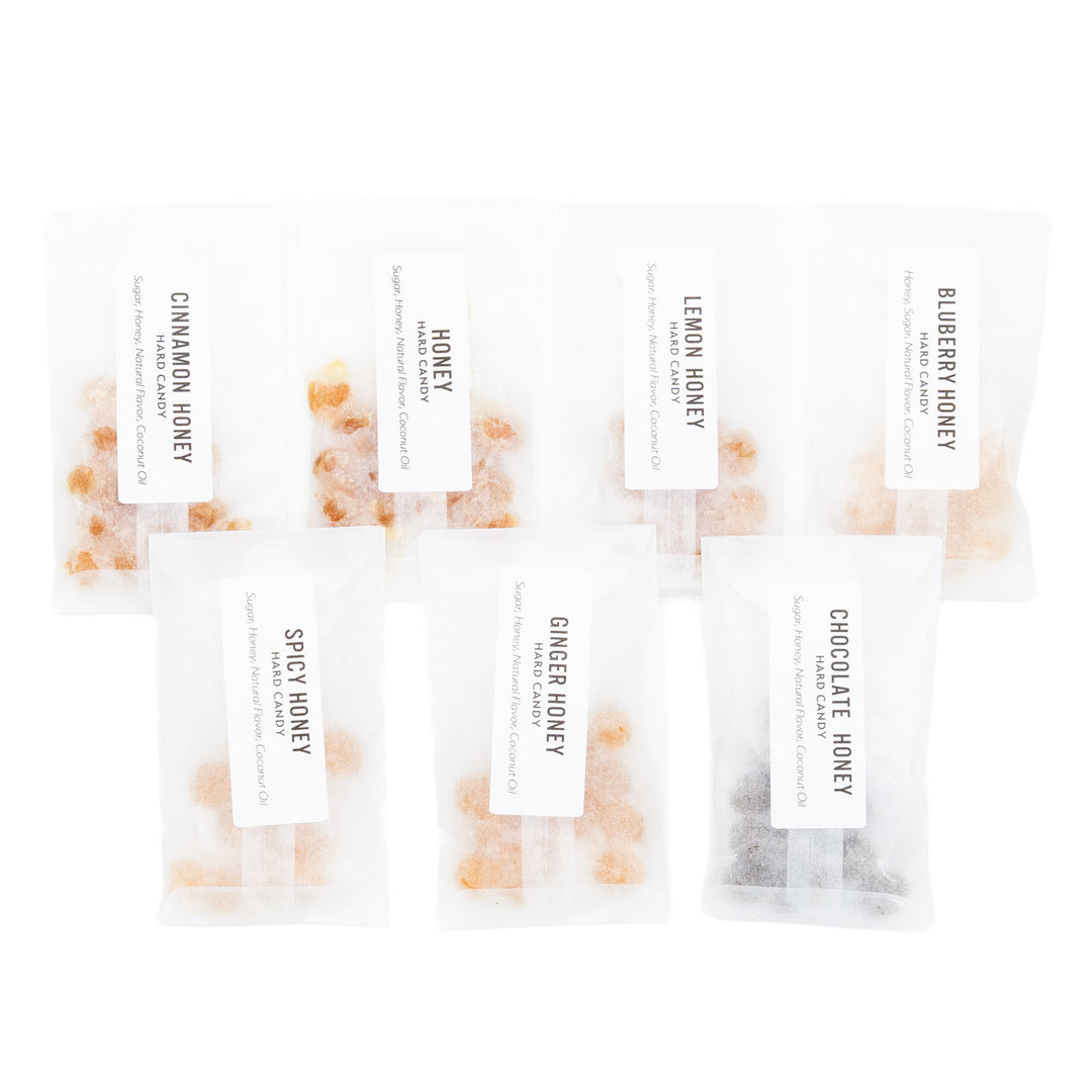 Six small clear resealable pouches of honey with white labels, arranged on a white background. The labels read Cinnamon Honey, Honey, Lemon Honey, Elberry Honey, Spicy Honey, and Ginger Honey.