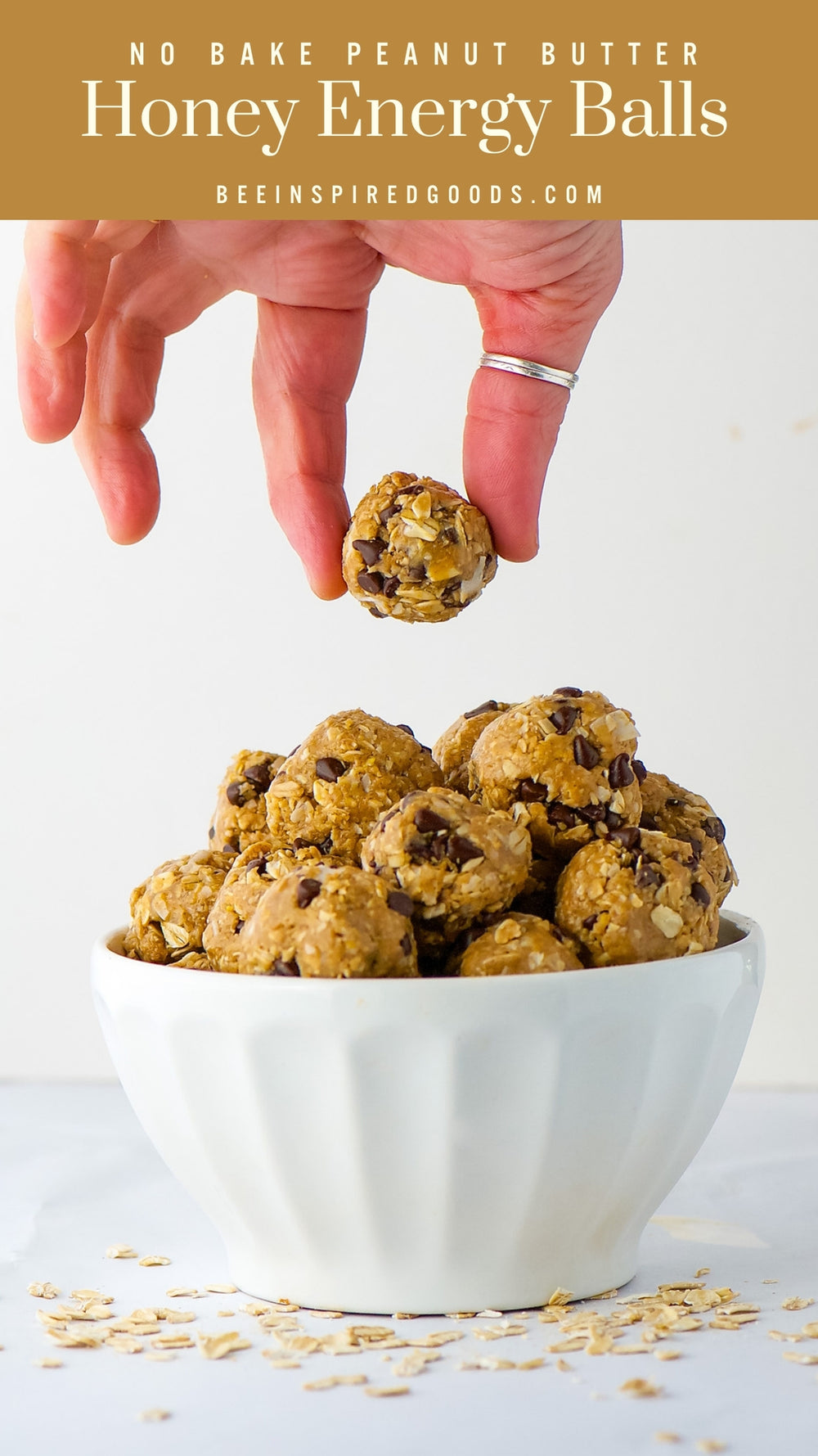 Hand holding a peanut butter honey energy ball above a bowl filled with similar balls on a light background.