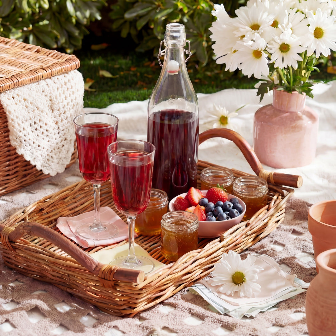 Picnic setup with wine glasses, bottle, and fruits on a blanket outdoors.