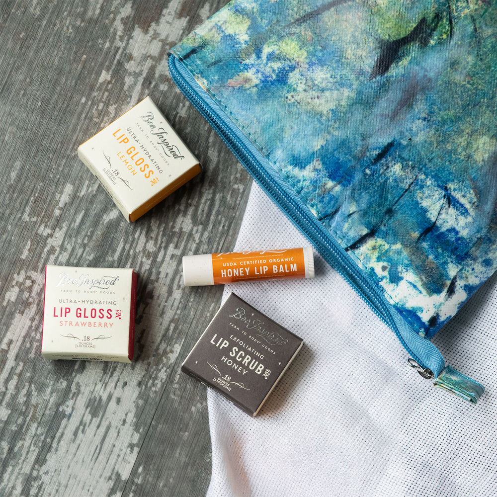 Collection of lip care products including lip gloss, balm, and scrub with a floral-patterned pouch on a textured surface.