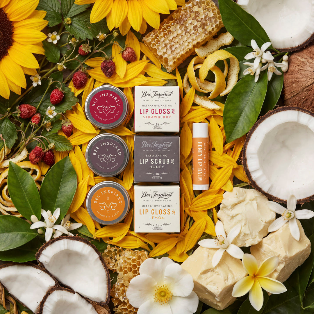 Collection of lip glosses, lip scrubs, and lip balms surrounded by sunflowers, coconuts, and flowers on a yellow background.