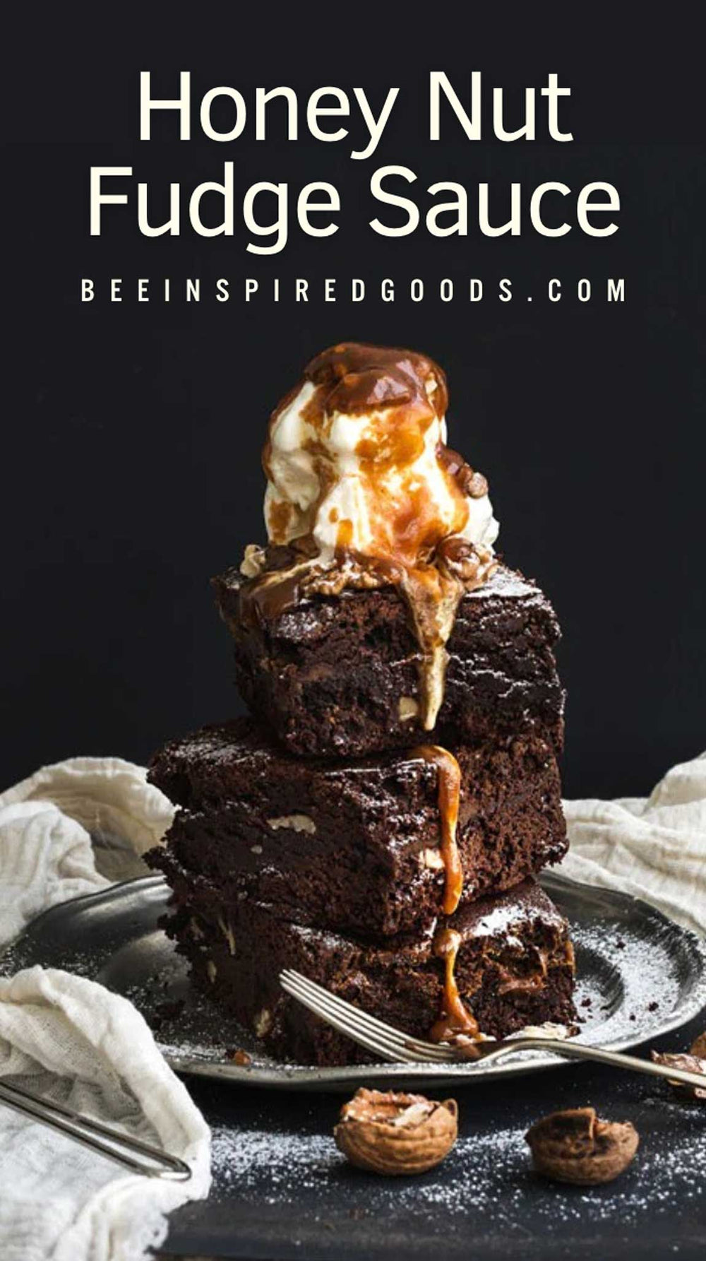 A tall stack of rich chocolate brownies topped with a swirl of vanilla ice cream and glossy caramel sauce, served on a plate with a fork. Large white text at the top reads 'Honey Nut Fudge Sauce' with 'BEEINSPIREDGOODS.