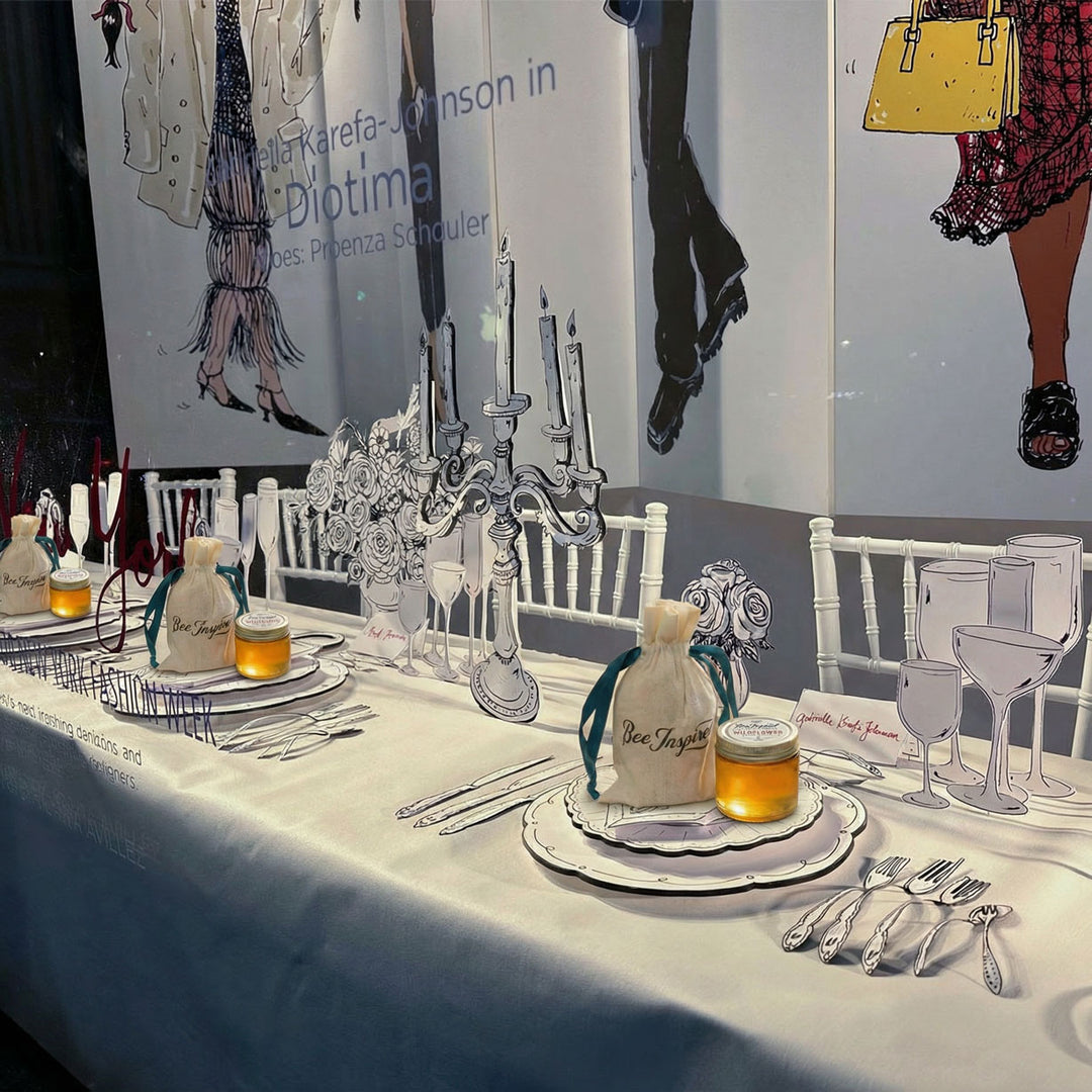 Decorated Berdorfs display table with 2-D plates, glasses, and cutlery against a backdrop of fashion illustrations featuring honey party favors

