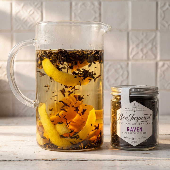 Clear pitcher with iced tea and lemon slices next to a jar of 'Bee Inspired' tea on a wooden surface.