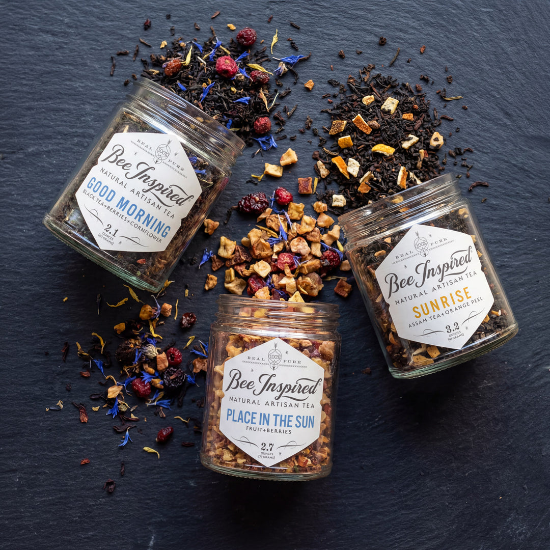 Three jars of Bee Inspired tea on a dark surface with loose tea leaves.