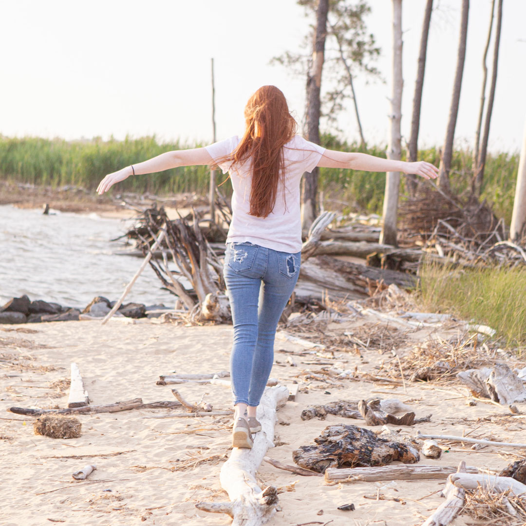 woman on a beach walking across a fallen tree