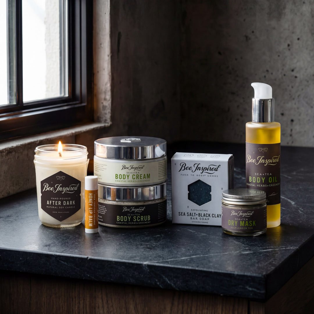Collection of Bee Inspired skincare and grooming products on a dark surface with a window in the background.