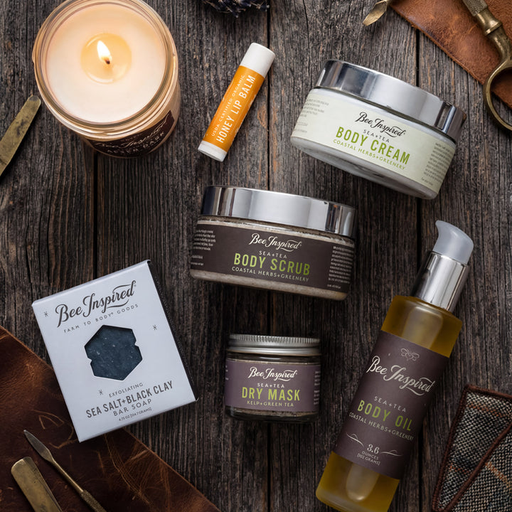 Collection of Bee Inspired skincare products on a wooden surface with a lit candle.