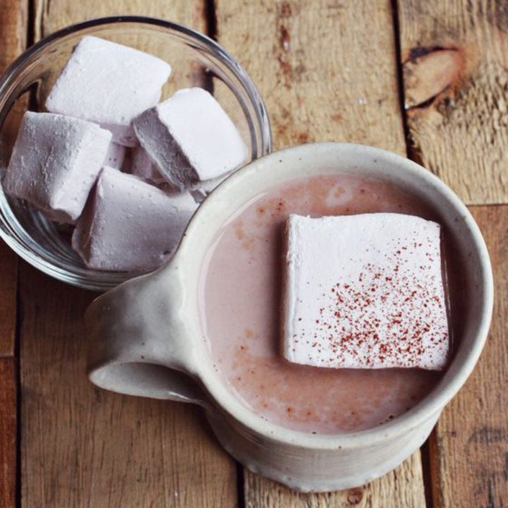 lavender marshmallow in a mug of hot chocolate next to a bowl with more lavender marshmallows