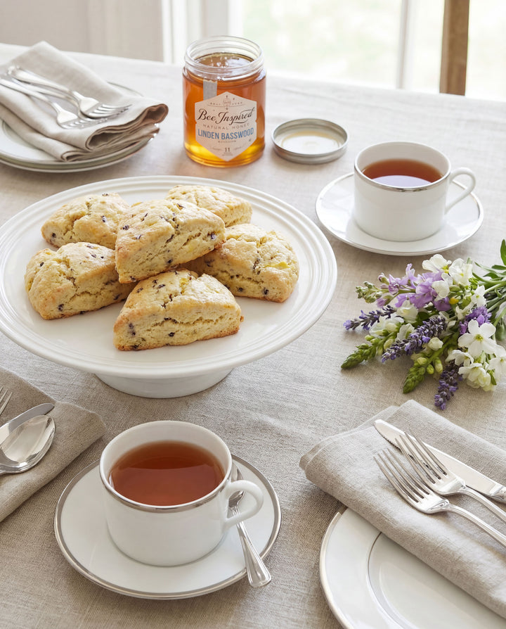 Tea time setting with scones, tea cups, and honey on a table.