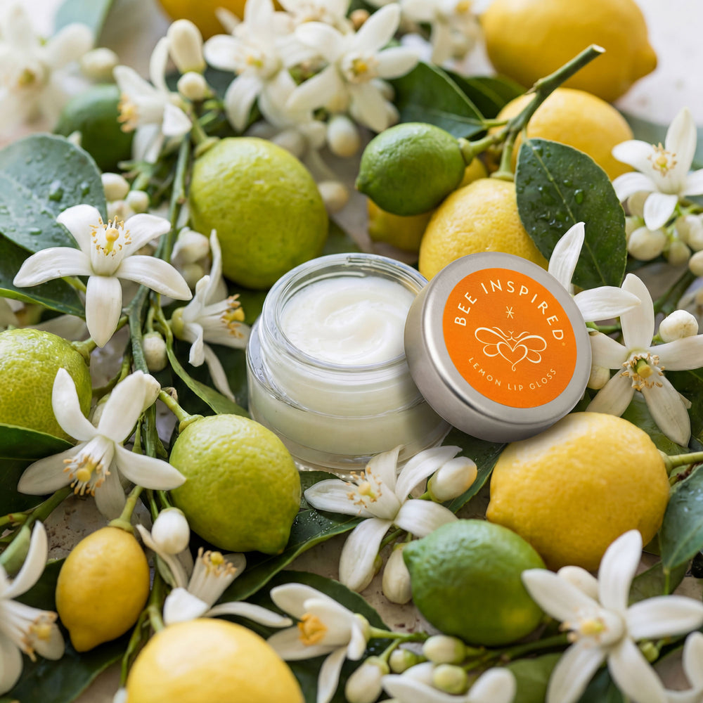 Cream jar with lid labeled 'Bee Inspired' surrounded by lemons, limes, and flowers.