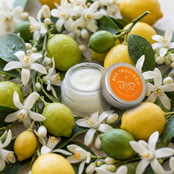 Cream jar with lid labeled 'Bee Inspired' surrounded by lemons, limes, and flowers.