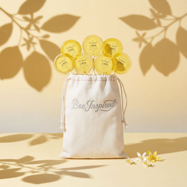 White drawstring bag labeled 'Bee Inspired' with yellow lemon-shaped products on a light background with leaf shadows.
