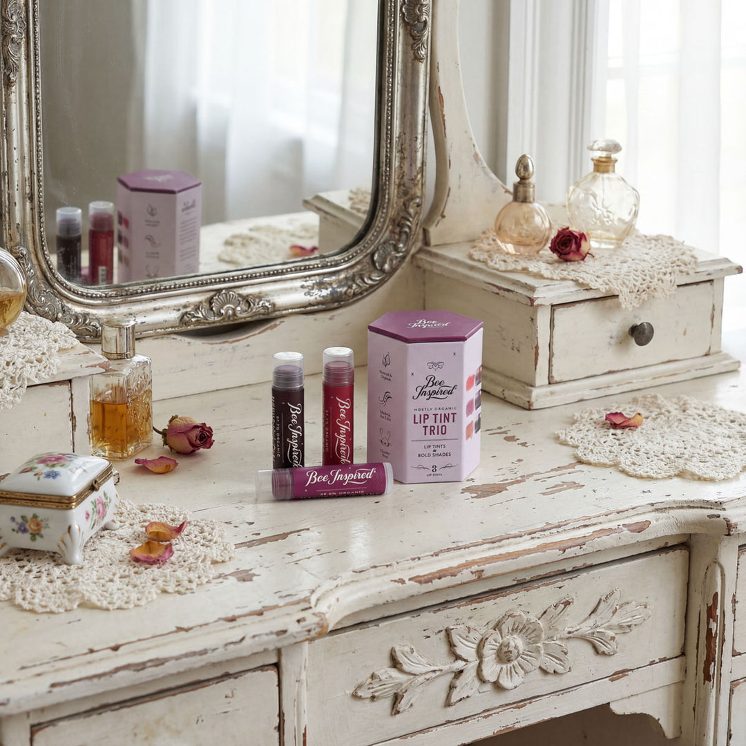 Vintage-style vanity with decorative mirror, lip tint trio, and perfume bottles on a distressed wooden surface.