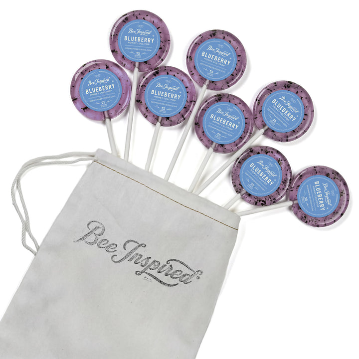 Purple lollipops with blue labels on sticks next to a 'Bee Inspired' drawstring bag.
