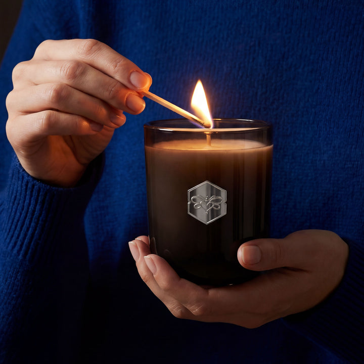 Person lighting a candle with a match, against a dark background