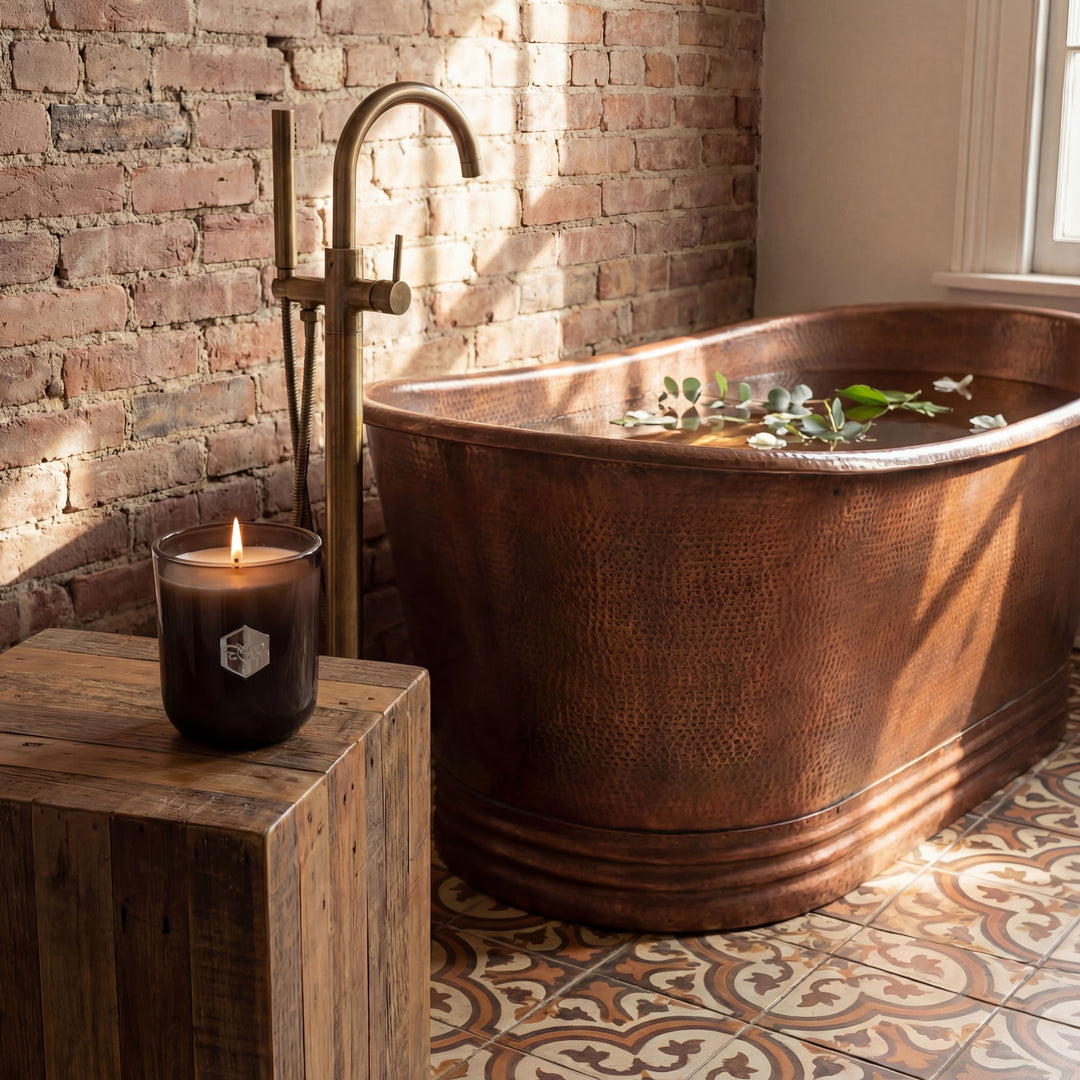 Copper bathtub with candles and flowers in a rustic bathroom setting.