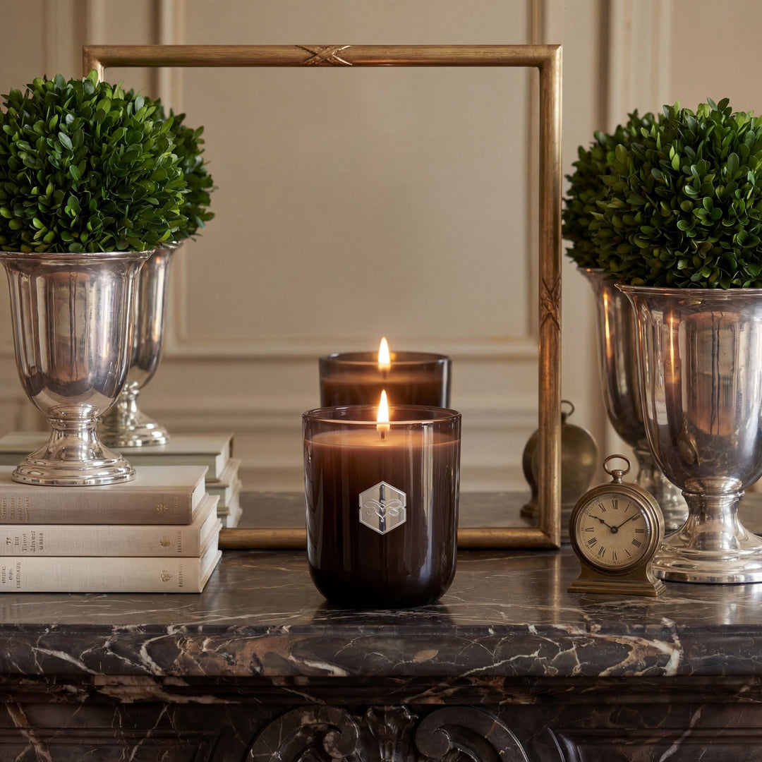 Decorative setup with candles, silver urns, books, and a clock on a marble surface.