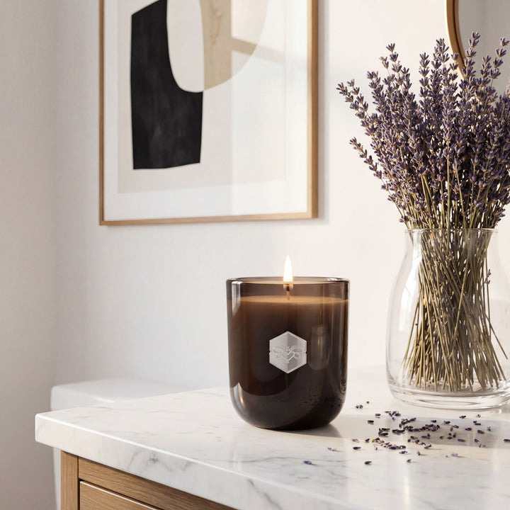 Candle with a hexagonal logo and lavender in a vase on a marble surface.