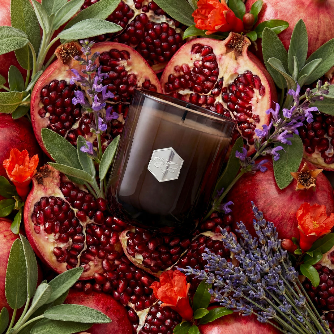 Candle with a geometric logo surrounded by pomegranates, flowers, and leaves
