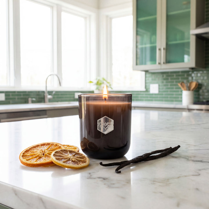Candle with a logo on a kitchen counter with vanilla beans and orange slices