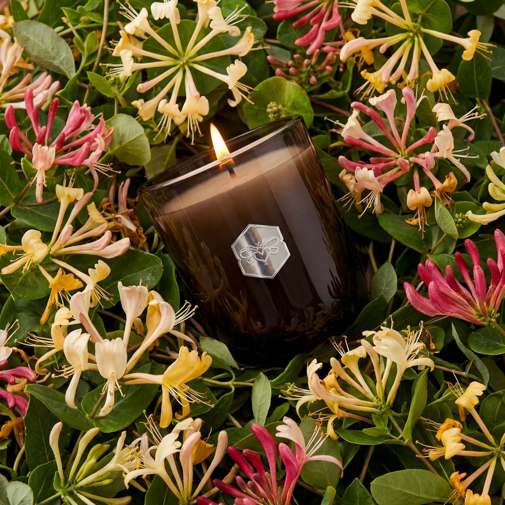 Candle with a brand logo surrounded by flowers and green leaves