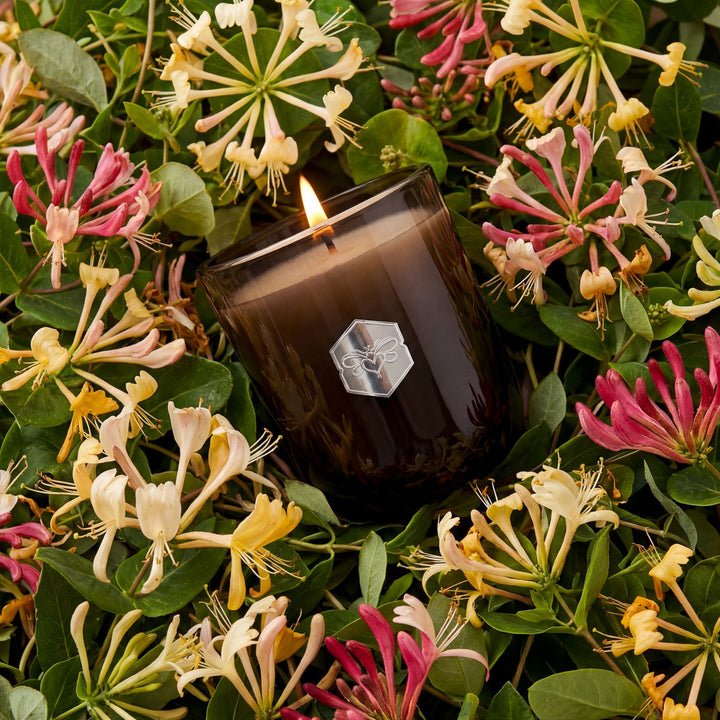 Candle with a brand logo surrounded by flowers and green leaves