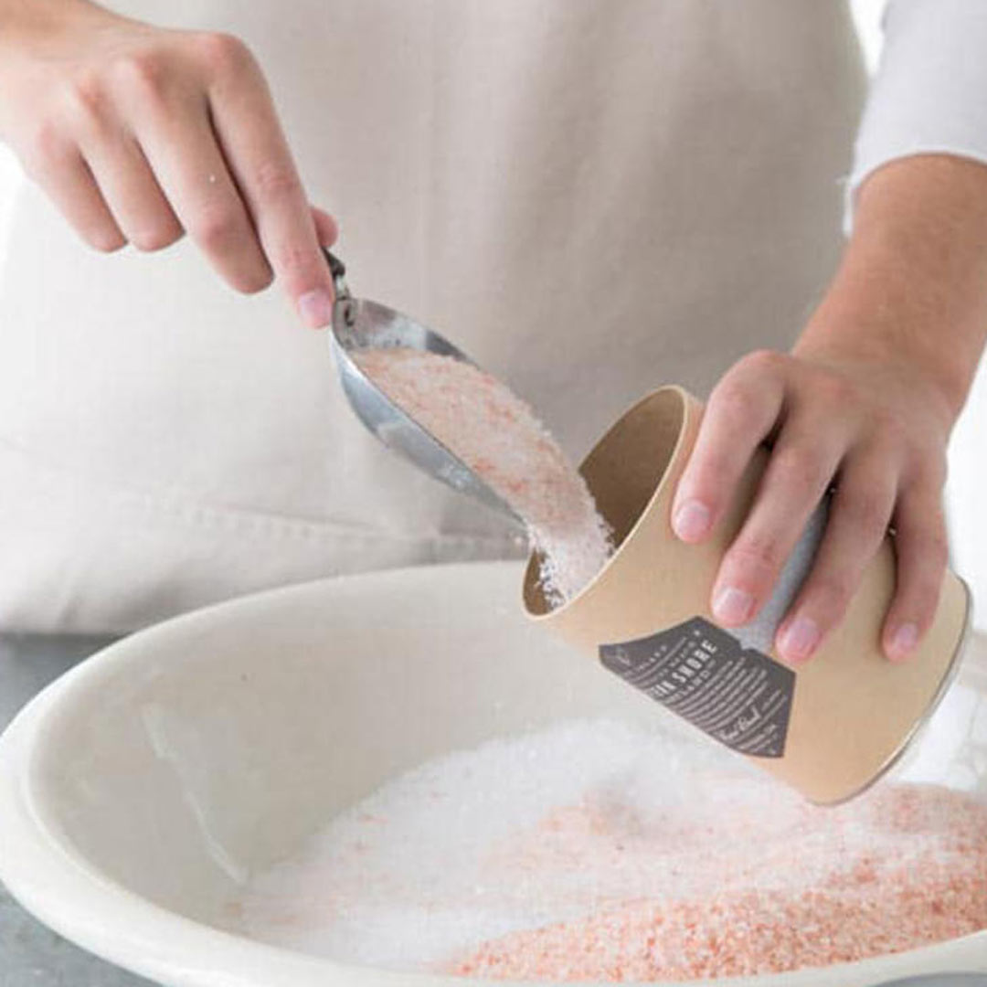 woman pouring bee inspired rose garden bath soak into a cardboard container