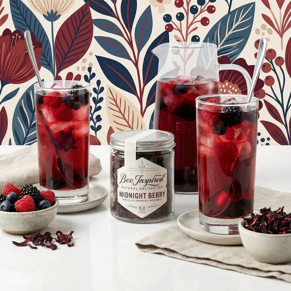 Two glasses of iced berry tea with a jar of 'Bee Inspired' Midnight Berry tea against a decorative floral background.
